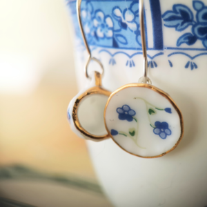 earrings made of tiny porcelain tea cups with forget me knots in blue and a gold edge